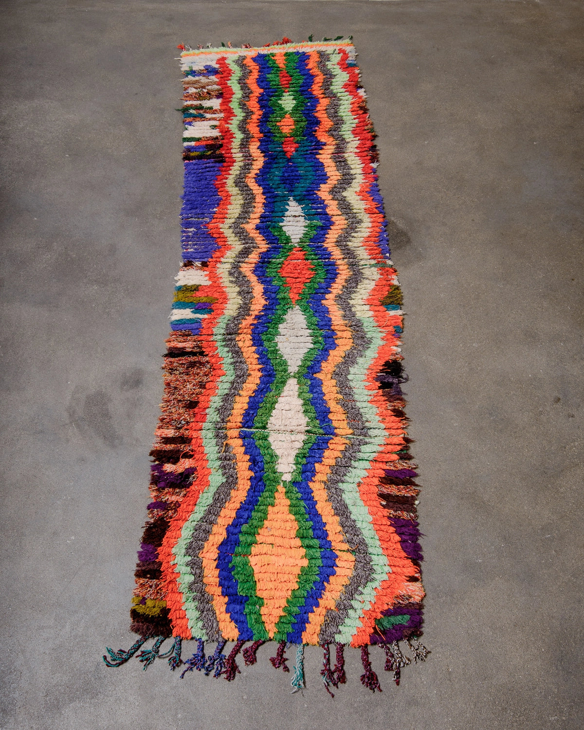 Berberlin Vintage Runner Rug made of recycled cloth and yarn in bright colours including blue, green, red and orange, photographed on concrete floor.